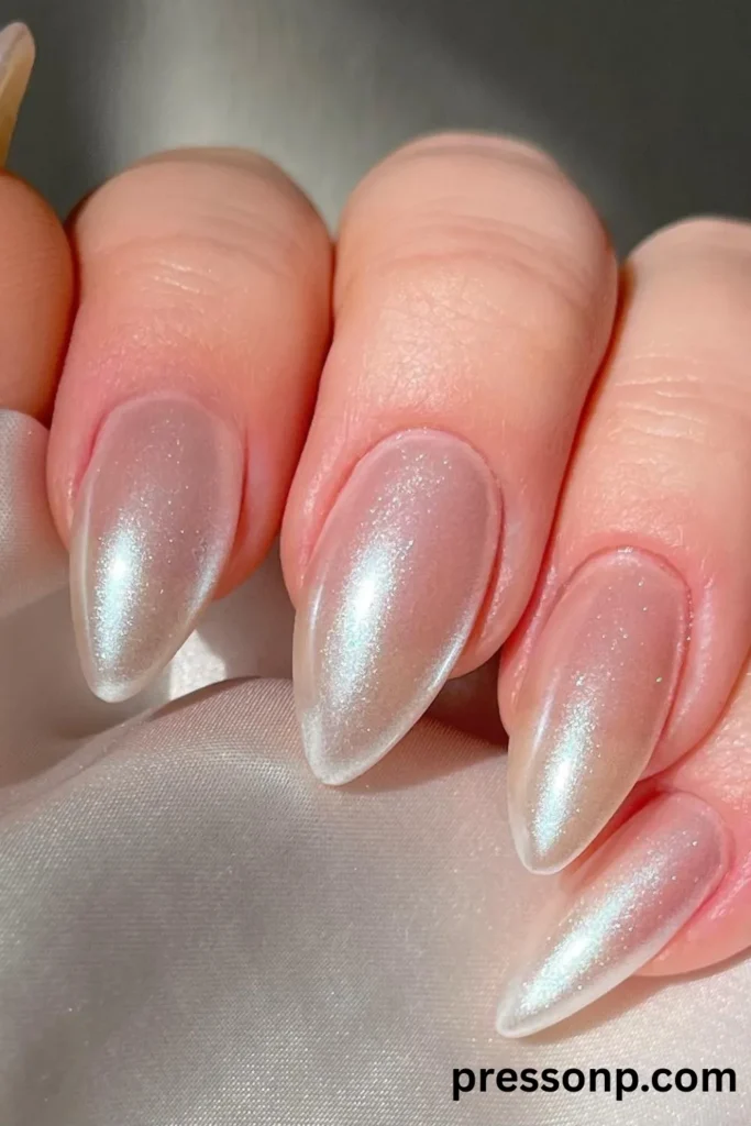 Close-up of long, almond-shaped nails coated in a shimmering iridescent pearl polish with a luminous silver-blue chrome glaze finish.