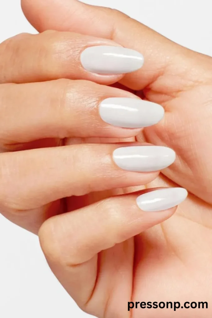 Close-up of elegant, oval-shaped nails painted in a solid, glossy creamy white polish against a clean white backdrop.