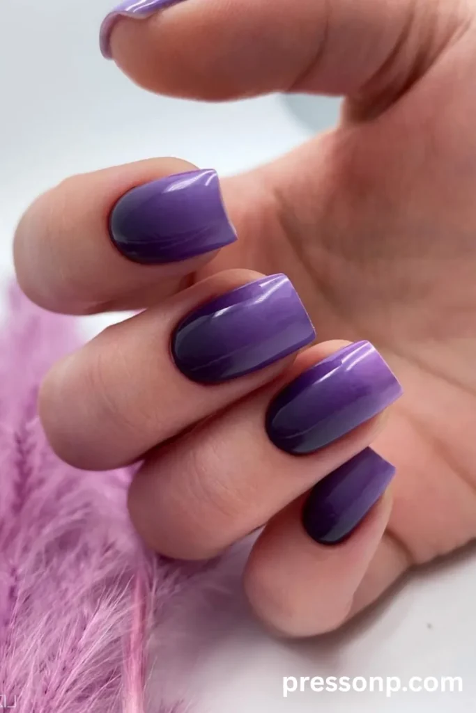Close-up of medium square acrylic nails featuring a high-gloss, deep royal purple aura or vertical ombre design that shifts into a lighter violet hue under a mirror-like shine.