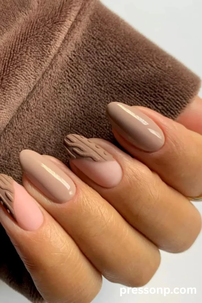 Close-up of almond-shaped nails in neutral brown tones, showcasing a mix of high-gloss taupe polish and a matte accent nail with a raised, 3D textured coconut shell pattern.