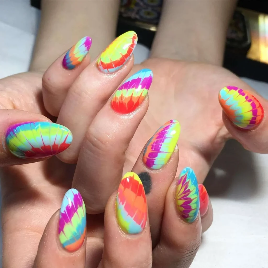 Close-up of long, rounded nails featuring a high-gloss, multi-colored tie-dye swirl manicure with vibrant neon stripes of pink, yellow, blue, and orange.