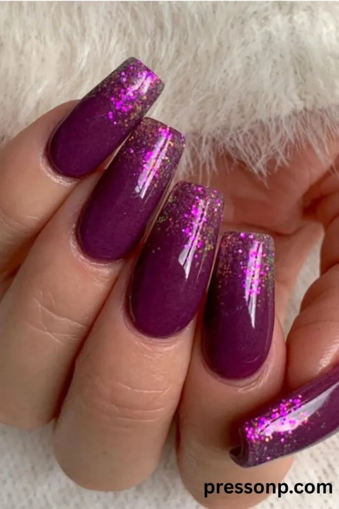 Close-up of long, square-shaped nails featuring a high-gloss deep berry purple polish accented with vibrant magenta and gold glitter gradients on the tips.