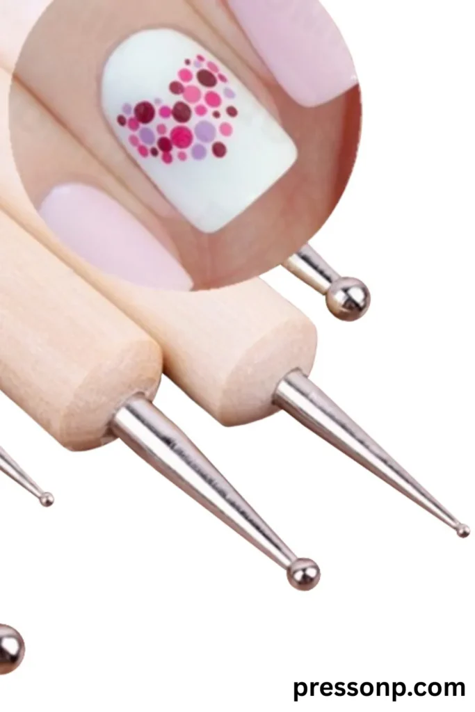 A graphic showcasing a set of wooden-handled metal nail art dotting tools with varying ball-tip sizes, paired with a circular inset image demonstrating a heart-shaped pattern made from colorful pink, purple, and maroon dots on a white natural nail.