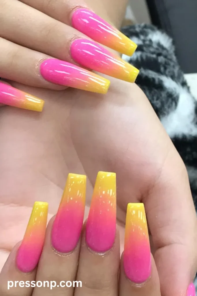 Close-up of long coffin-shaped nails featuring a bright ombre gradient that transitions from a vivid neon pink base into an electric orange-yellow pop at the tips.