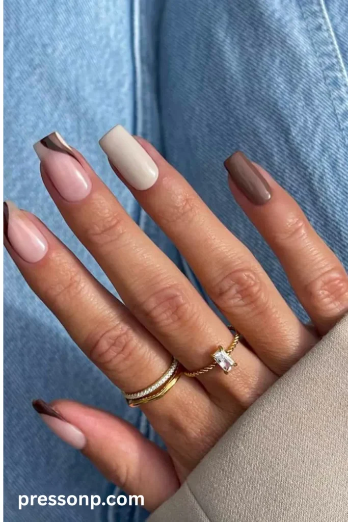 A close-up of a hand showcasing a modern "espresso and cream" neutral manicure on long square nails, featuring alternating solid shades of rich brown and soft beige alongside sheer nails with abstract dark brown swirls.