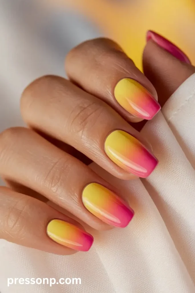 Close-up of medium-length squoval nails featuring a vibrant sunset ombré gradient transitioning from bright yellow at the base to intense pink at the tips with a high-gloss finish.