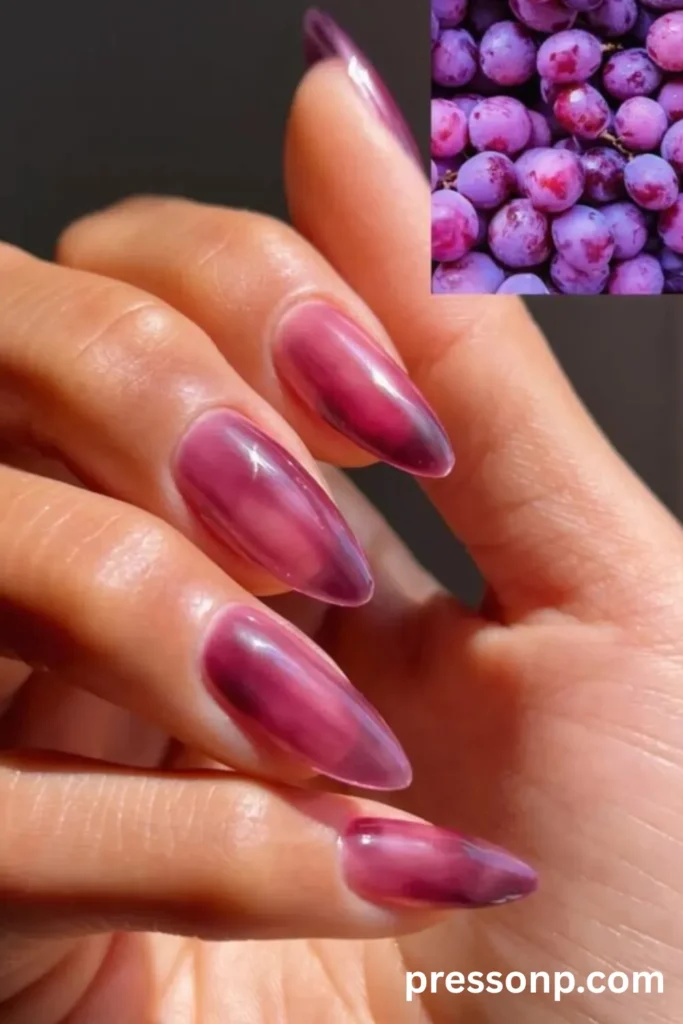 Close-up of long almond-shaped nails featuring a translucent, high-gloss grape purple jelly polish with a glass-like finish, accompanied by an inset image of purple grapes.