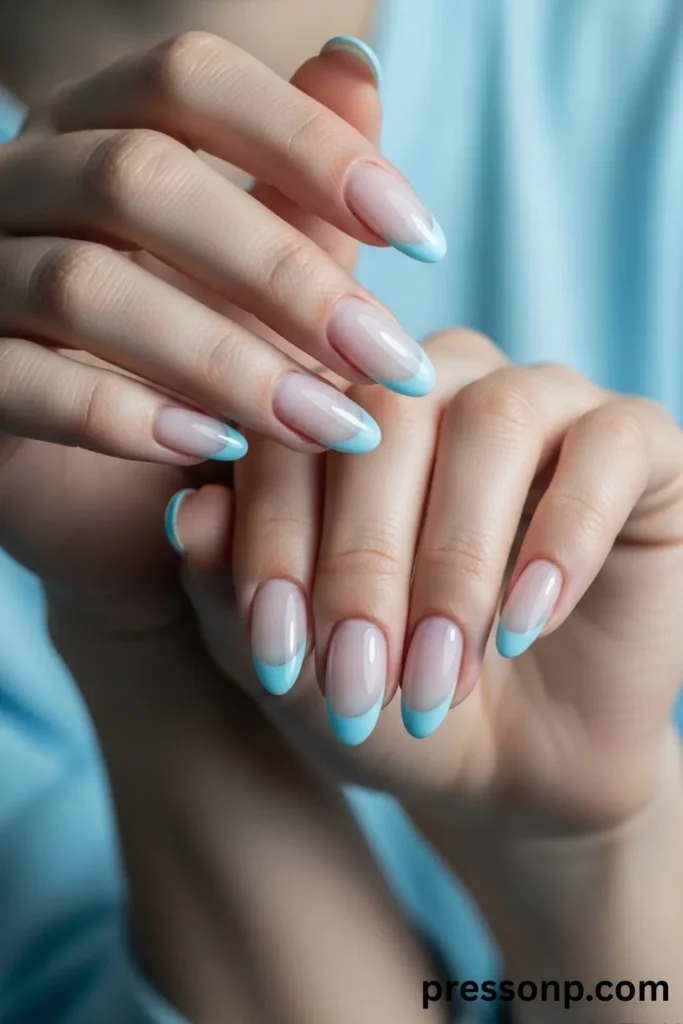 A close-up of a pair of hands displaying an elegant, high-gloss French tip manicure on long almond-shaped nails, featuring a sheer, natural nude-pink base paired with crisp, pastel sky-blue crescent tips.
