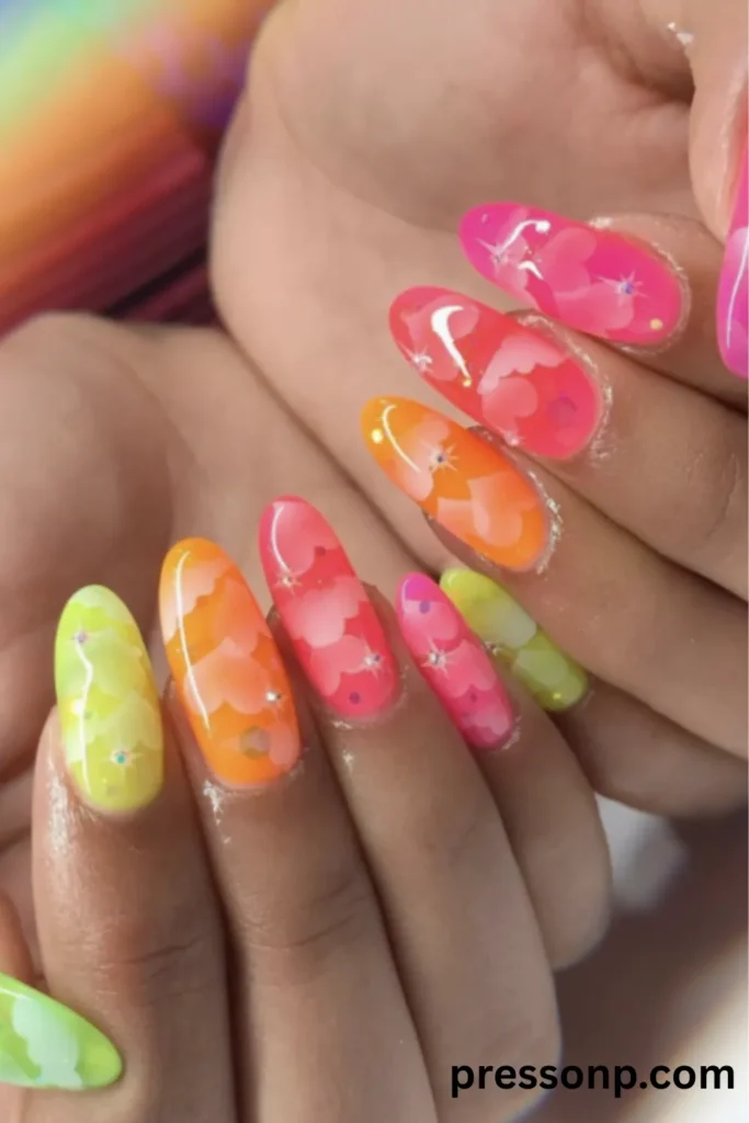 Close-up of long oval nails featuring a bright multi-colored jelly manicure in shades of pink, orange, yellow, and green, decorated with layered cloud nail art and tiny sparkling star glints.