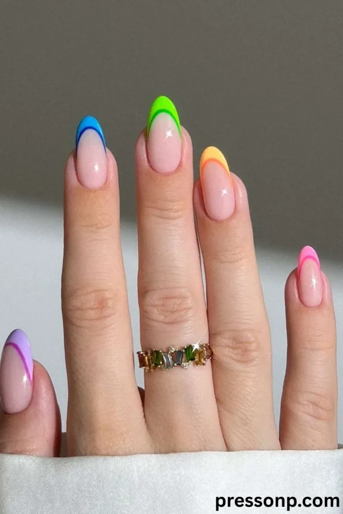 A close-up of a hand displaying a vibrant rainbow "skittle" French manicure on medium oval nails, featuring a high-gloss nude base with dual-toned, neon-rimmed French tips in purple, blue, green, orange, and pink.