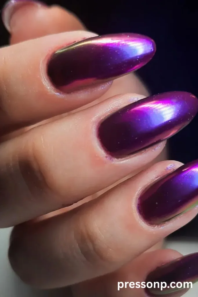Close-up of long, rounded oval nails featuring a metallic chrome finish that shifts from deep lavender to vibrant violet and holographic green.