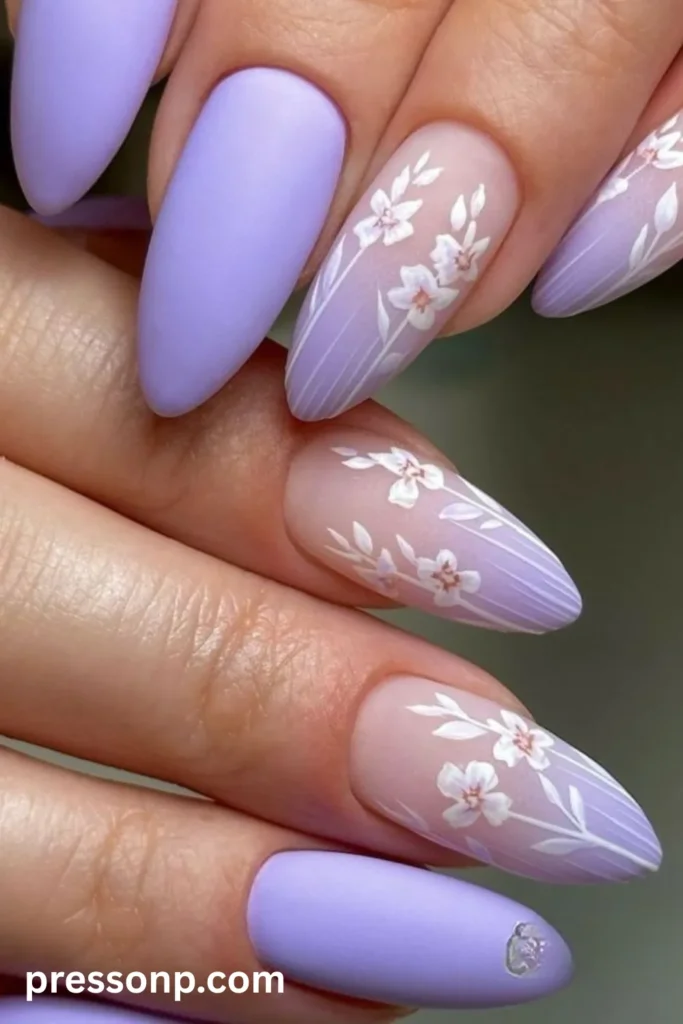 Close-up of long almond-shaped nails showcasing a matte lavender polish mixed with sheer accent nails decorated with elegant hand-painted white floral designs.