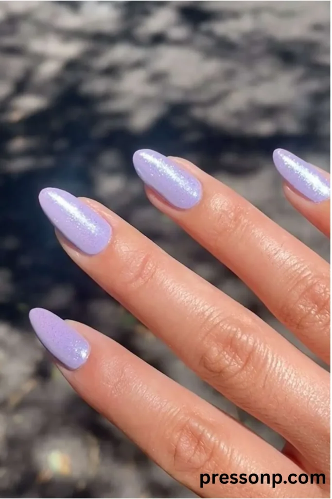 Close-up of long almond-shaped nails painted in a solid pastel lavender purple polish with a luminous silver shimmer finish.