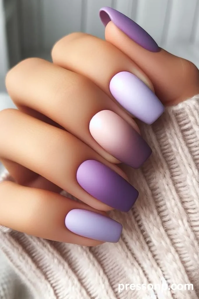 Close-up of long square nails with a smooth matte finish, featuring a skittles-style layout of purple shades and vertical ombre gradients in lavender, lilac, and plum.