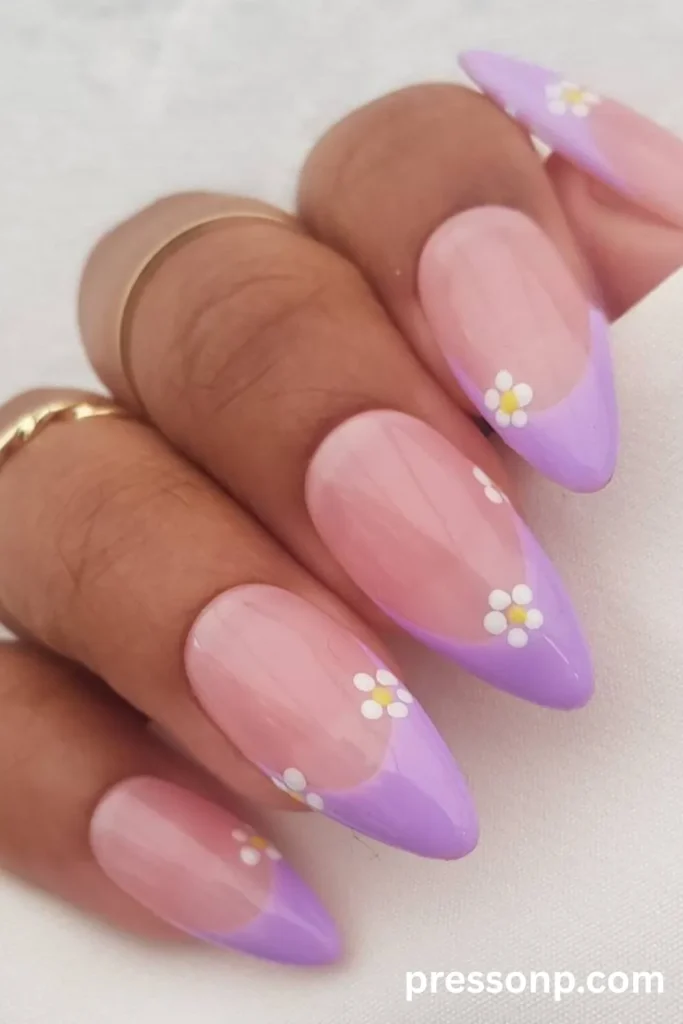 Close-up of long almond-shaped nails featuring a natural nude base with glossy lilac French tips, delicately decorated with small white and yellow daisy floral accents along the smile lines.