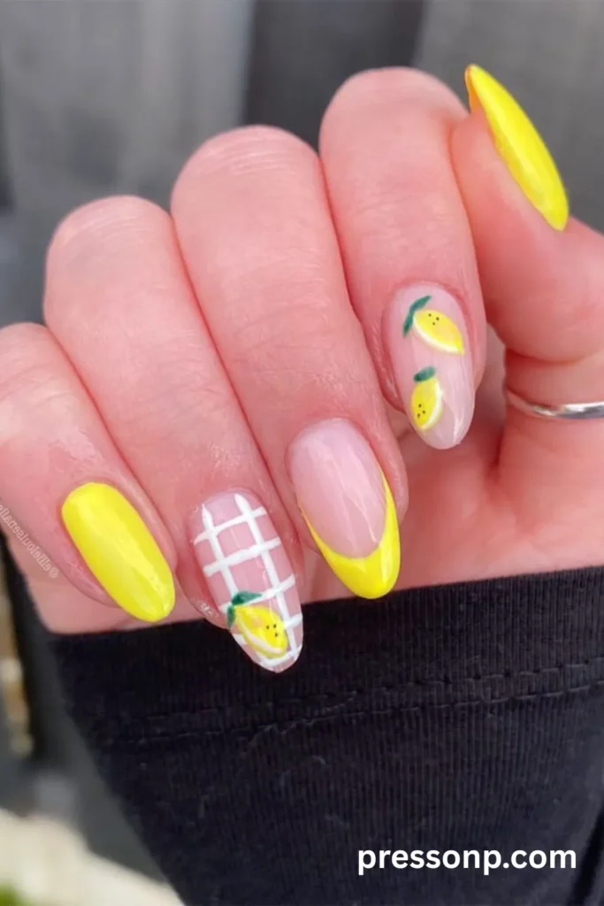 A close-up of a hand displaying a vibrant, zesty lemon-themed manicure on medium oval nails, featuring a mix of solid bright yellow lacquer, a bold yellow French tip, a white gingham plaid accent nail, and delicate hand-painted lemons over a sheer base.