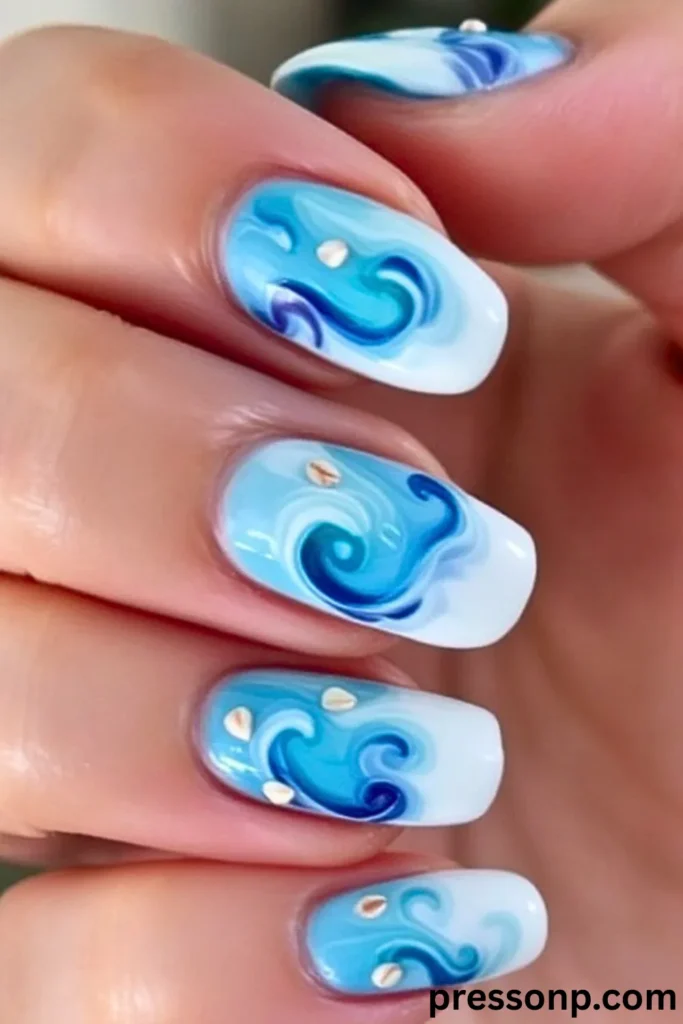 A close-up of a hand displaying long, squoval extensions with a glossy, hand-painted ocean wave manicure, featuring fluid blue, turquoise, and white marbled swirls accented with tiny embedded seashell fragments.