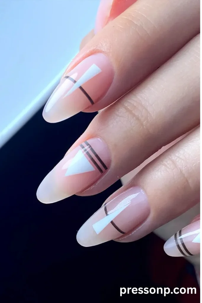 Close-up of long almond-shaped nails featuring a translucent matte  base decorated with stark white triangles and sharp, glossy black geometric lines