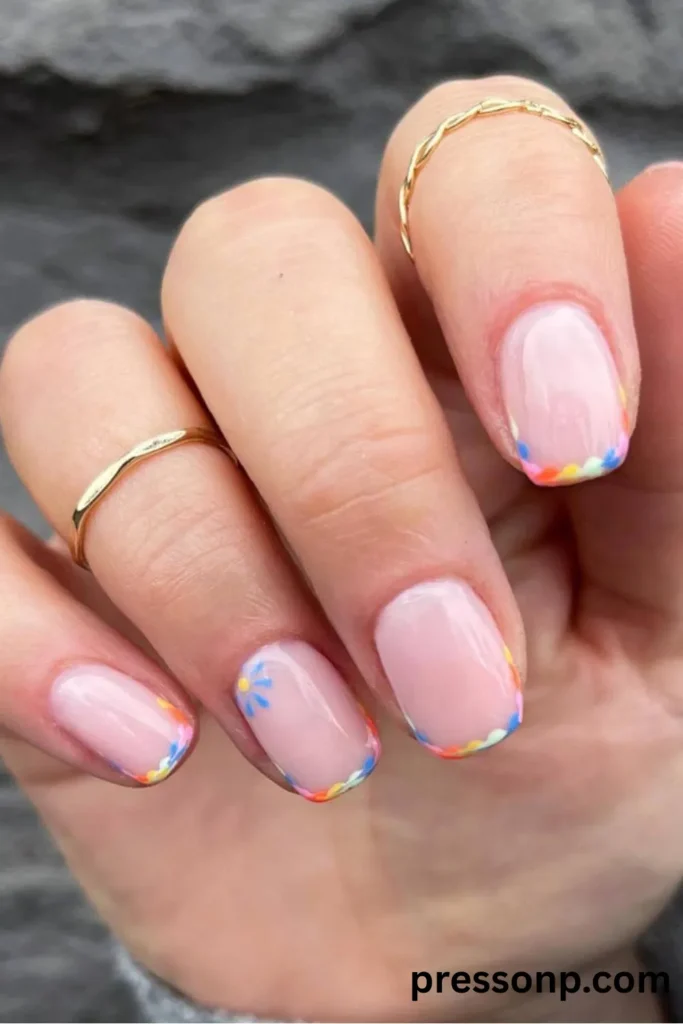 Close-up of short, glossy squoval nails featuring a sheer nude base and an ultra-thin, multi-colored rainbow micro-French tip design with a tiny daisy accent.