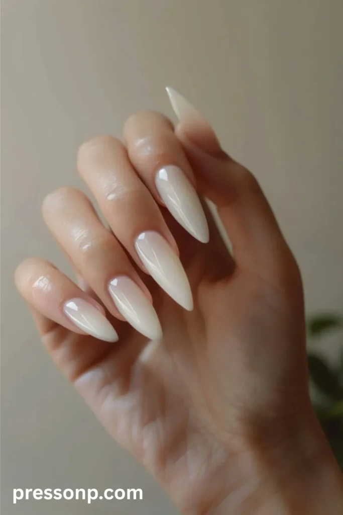 Close-up of long stiletto-shaped nails painted in a solid, semi-translucent milky white polish with a flawless high-gloss finish.