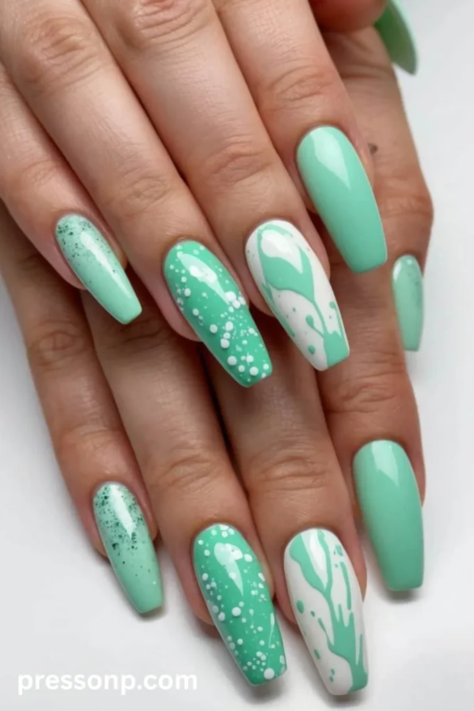 Close-up of long coffin-shaped nails showcasing a mix-and-match mint green and white manicure with glossy solid colors, abstract paint splatters, and speckled glitter accents.