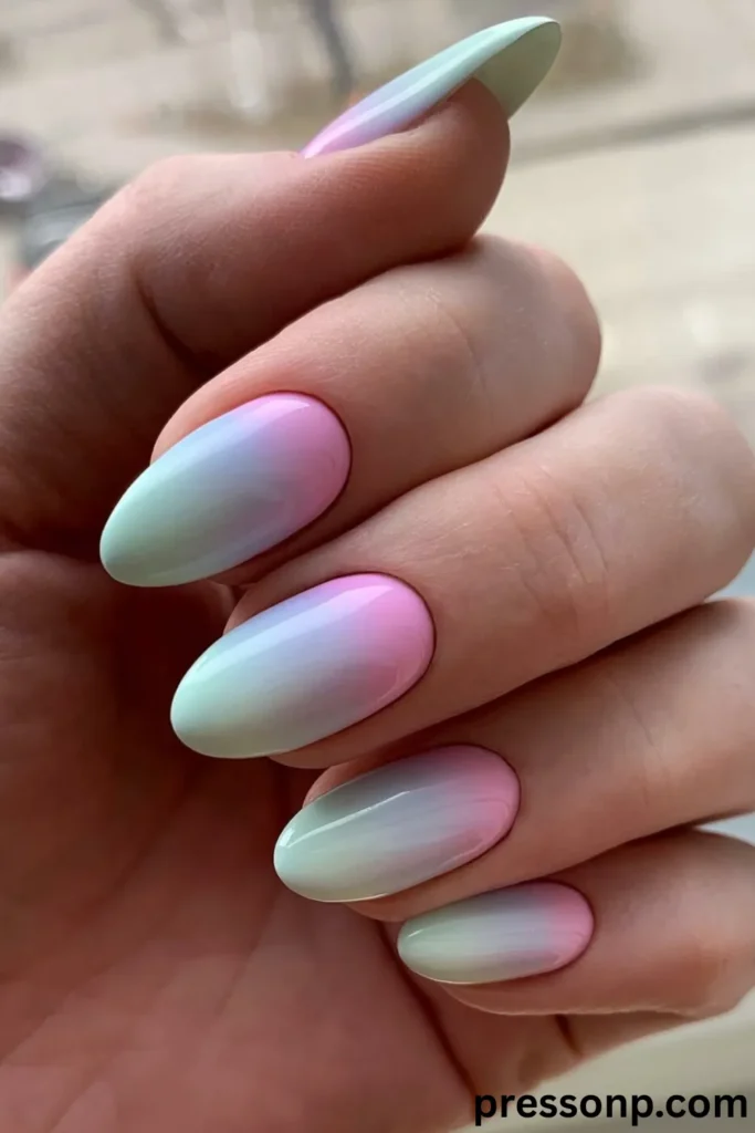 A close-up of a hand displaying an all-over pastel vertical ombré manicure on medium almond-shaped nails, seamlessly transitioning across the nail beds from a soft candy pink at the cuticles to a light mint green at the tips.