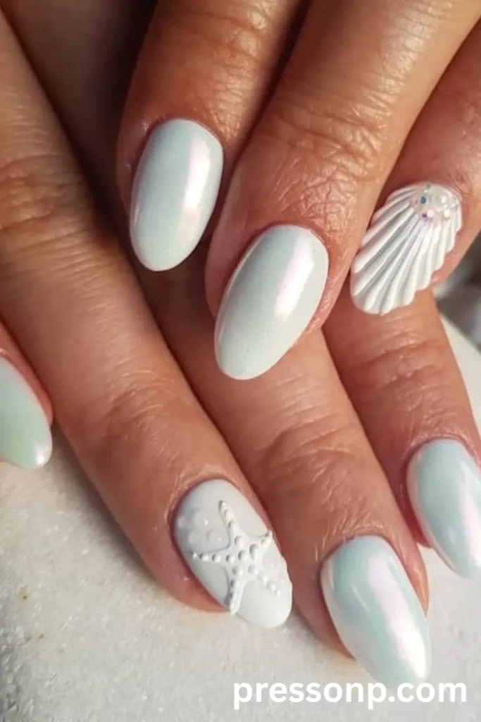 A close-up of a hand displaying short to medium oval nails with a luminous white chrome finish, featuring textured 3D accent art including a sculpted white seashell with pearls and a raised matte white starfish.