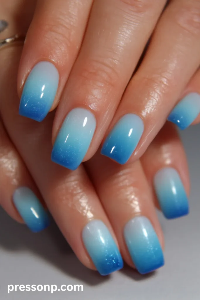 Close-up of medium-length square nails featuring a flawless ocean blue ombré gradient that transitions from a milky white base to a deep blue tip with a glossy, shimmering finish.