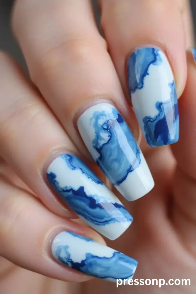 Close-up of long, slightly rounded square acrylic nails with a crisp white base, featuring a glossy abstract marble design resembling ocean waves in shades of royal blue, teal, and soft sky blue.