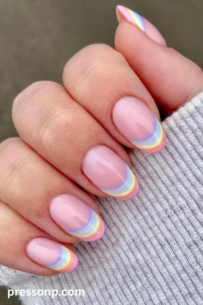 Close-up of medium almond-shaped nails featuring a translucent nude base finished with delicate, multi-colored pastel rainbow French tips in a soft striped pattern.