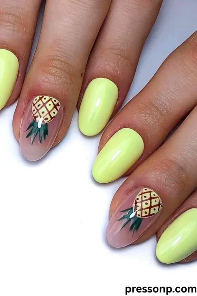 A close-up of a manicure featuring medium oval nails coated in a bright, glossy pastel yellow lacquer, paired with translucent nude accent nails that display hand-painted pineapple illustrations near the cuticles.