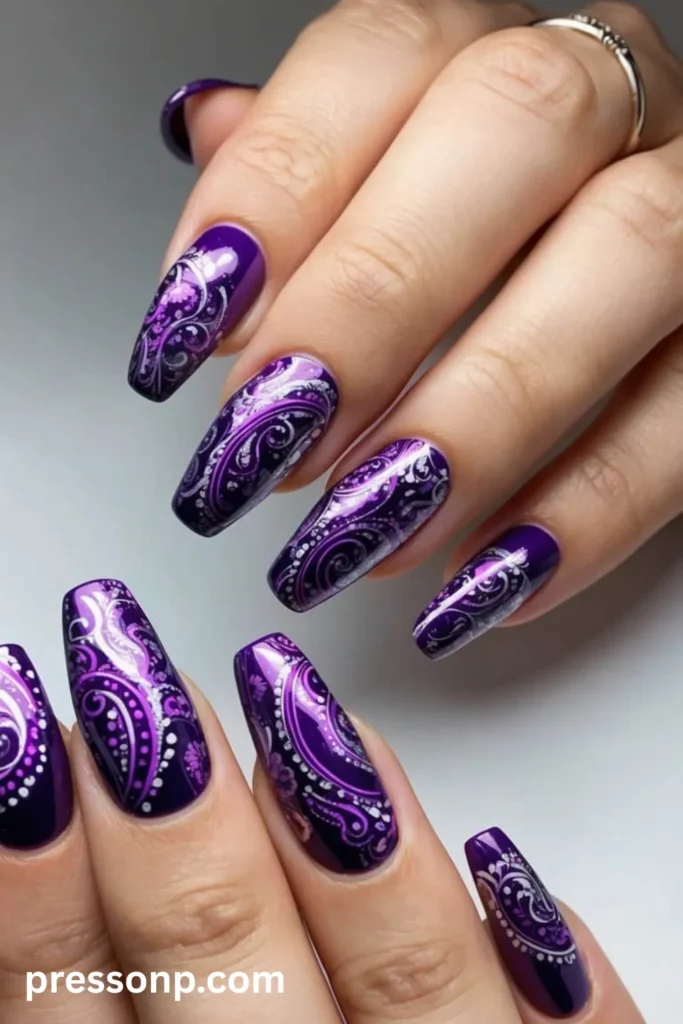 Close-up of long, glossy coffin-shaped nails painted in a deep royal purple, featuring an intricate silver chrome paisley and swirl pattern with a high-shine metallic finish.