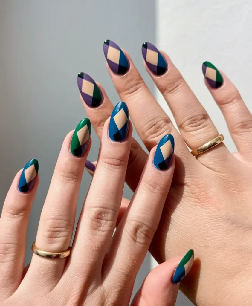 Close-up of long almond nails decorated with a matte geometric color block design featuring an argyle pattern of turquoise, purple, green, black, and beige diamonds.