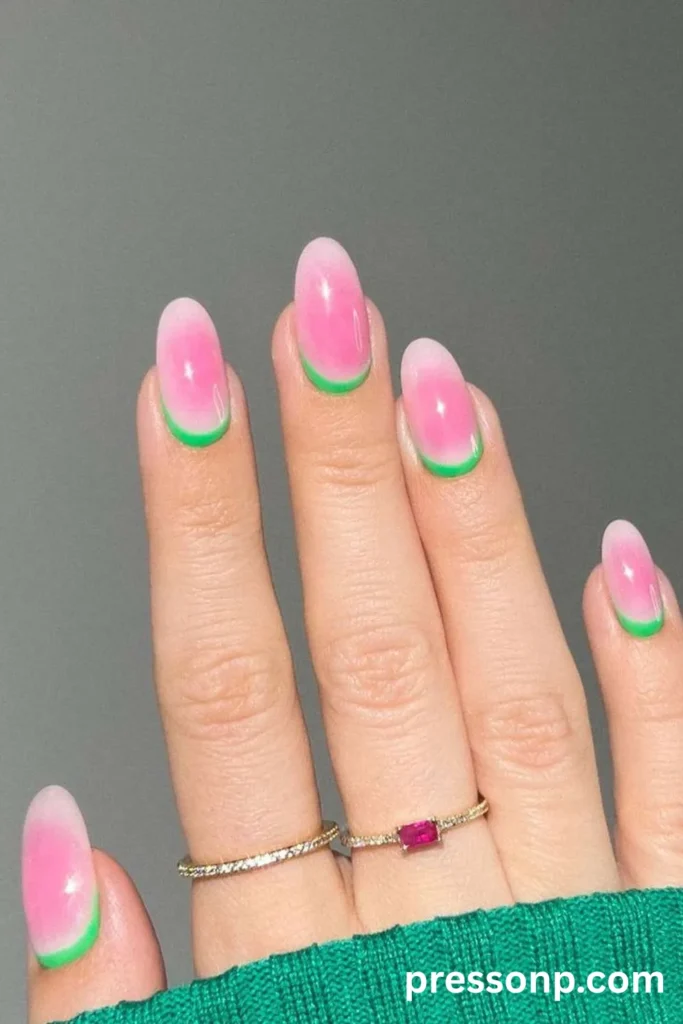 Close-up of long oval nails featuring a pink aura glow design and a reverse French manicure outline along the cuticles in bright neon green.