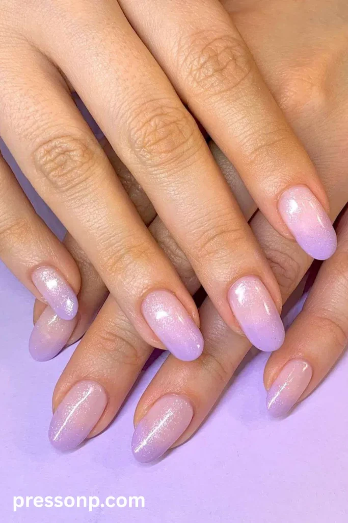 Close-up of long oval-shaped nails showcasing a soft, sheer lavender-purple ombré gradient coated with a dusting of fine silver shimmer.