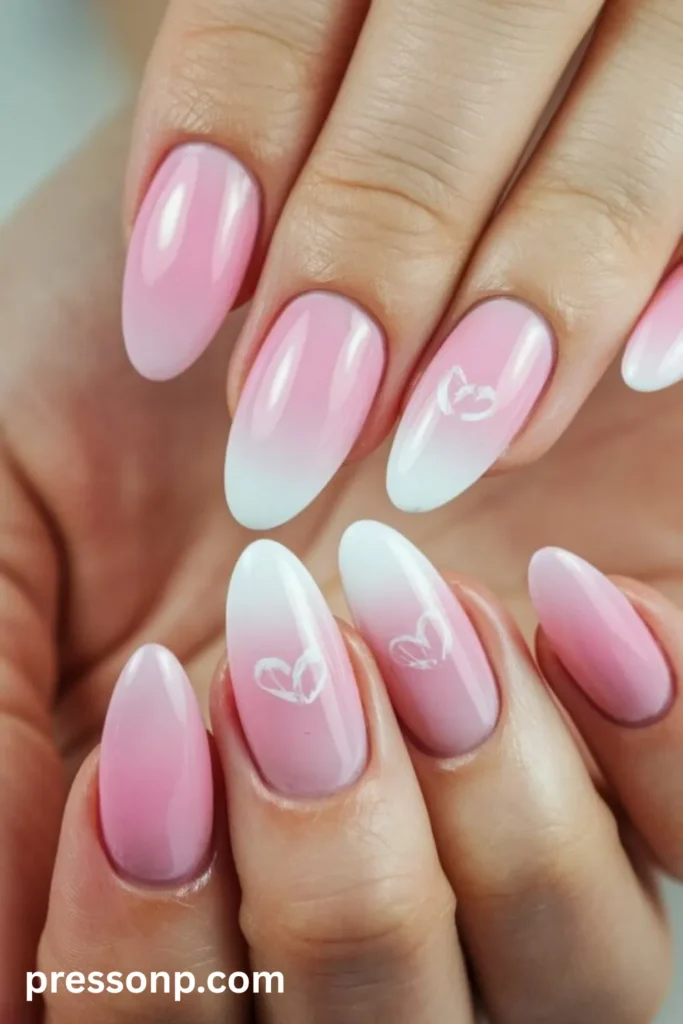 Close-up of long oval nails featuring a smooth soft pink to white ombré gradient, decorated with minimalist white heart accent nail art.