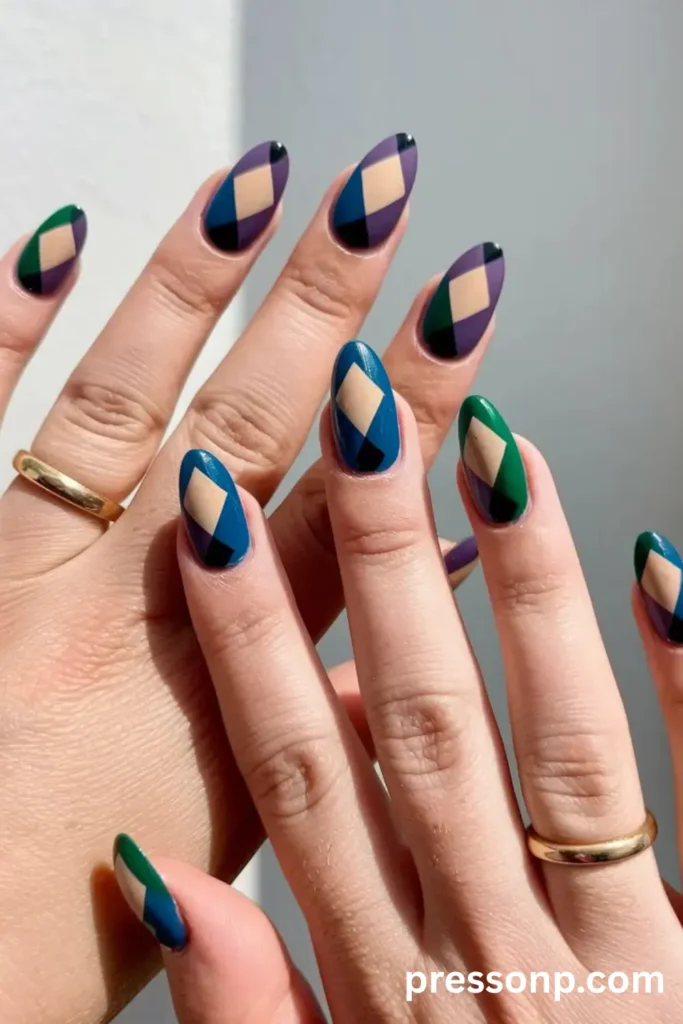 Close-up of two hands showing long oval nails with a split-tone color blocking argyle design in matte shades of teal, purple, emerald green, beige, and black.