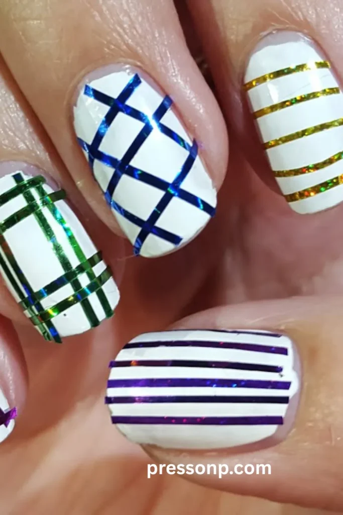 A close-up photograph of a hand displaying a geometric manicure on short oval nails, featuring a crisp white base decorated with different patterns of metallic, holographic striping tape in vibrant blue, green, purple, and gold.