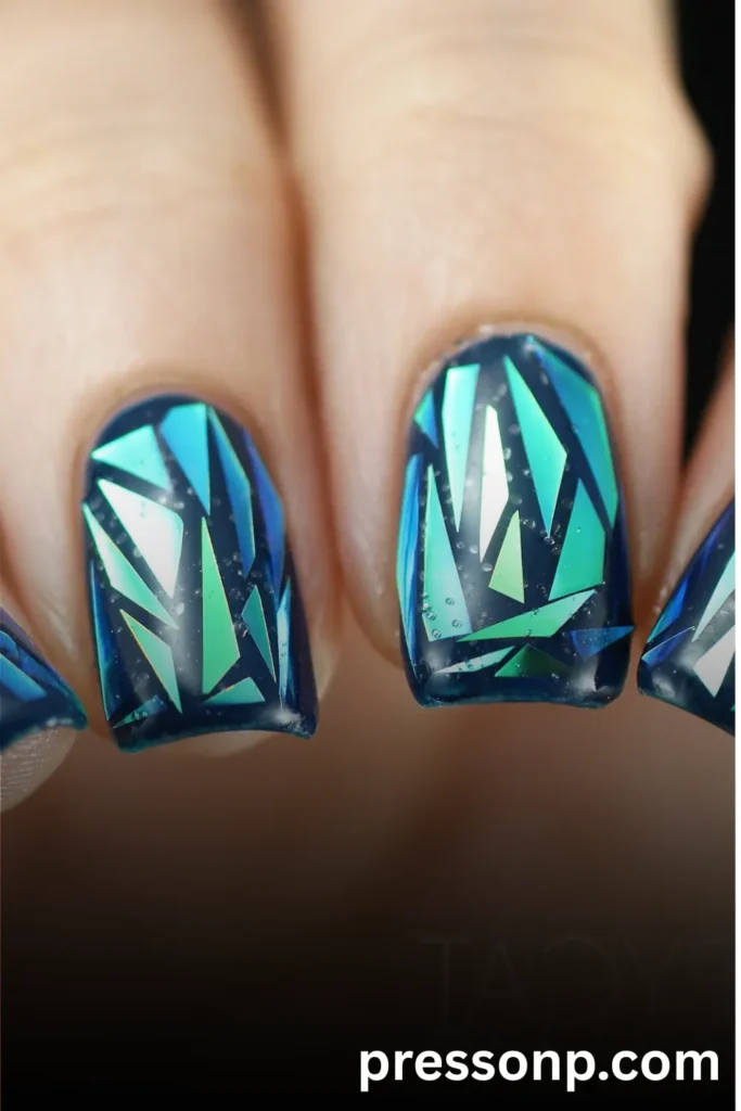 A macro close-up of square-shaped nails featuring a deep navy blue base decorated with an intricate "broken glass" mosaic pattern made of iridescent teal, aqua, and green cellophane shards that mimic shimmering ocean waves.
