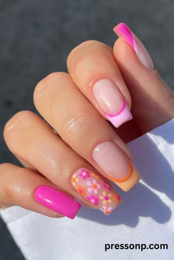 A close-up photograph of a hand showcasing a vibrant, retro summer manicure on long square nails, featuring mismatched abstract French tips in shades of hot pink and pastel orange, paired with a colorful matte daisy flower accent nail.