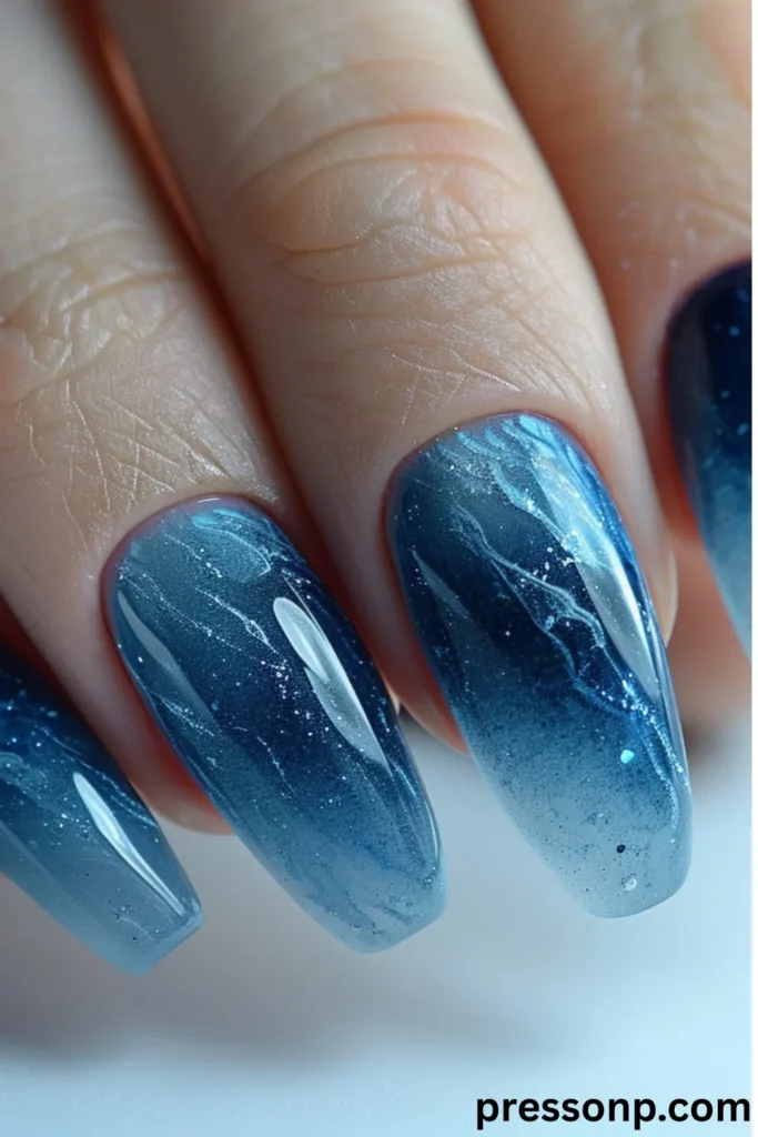 close-up of long, coffin-shaped extension nails featuring a high-gloss ocean ombré manicure that transitions from a deep midnight blue at the cuticles to a translucent seafoam blue at the tips, detailed with shimmering cat-eye effects and white quartz wave marbling.