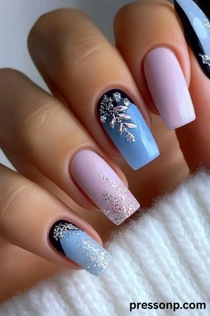 A close-up of a hand displaying an intricate winter-themed manicure on long squoval nails, featuring alternating shades of pastel lavender and slate blue gel polish decorated with fine silver glitter gradients, black cuticle frames, and 3D gemstone rhinestone leaf art.