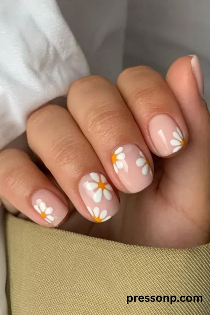 Close-up of short, square-shaped manicured fingernails featuring a romantic floral design with hand-painted white and yellow daisies over a sheer, glossy nude base coat.