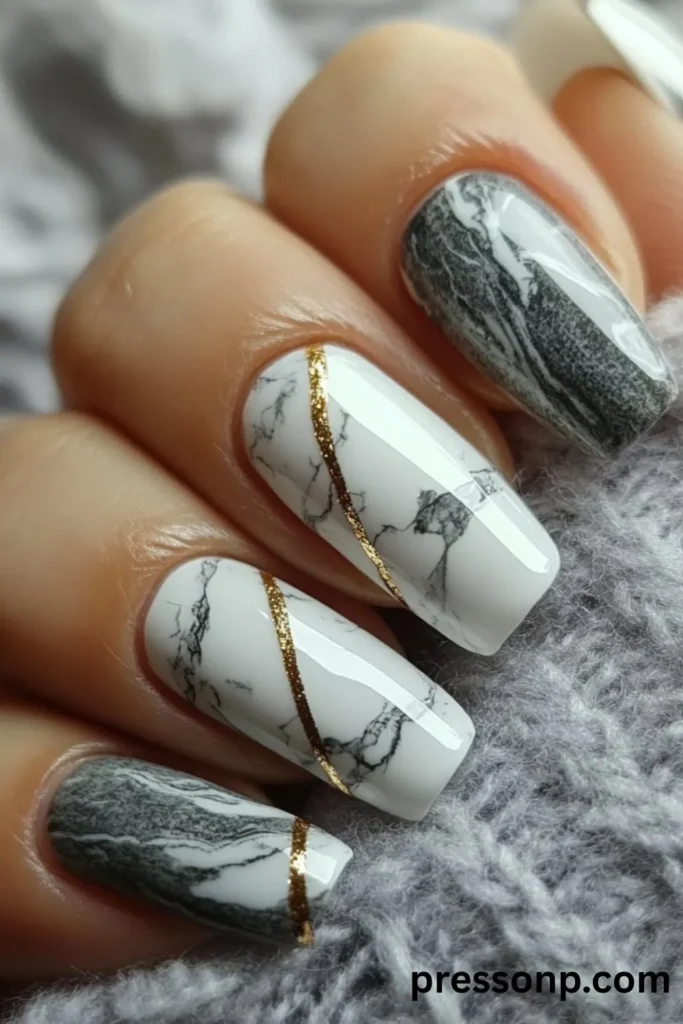 Close-up of long squoval nails featuring a high-gloss white marble texture accented with metallic gold glitter lines, alongside contrasting dark gray marble accent nails.