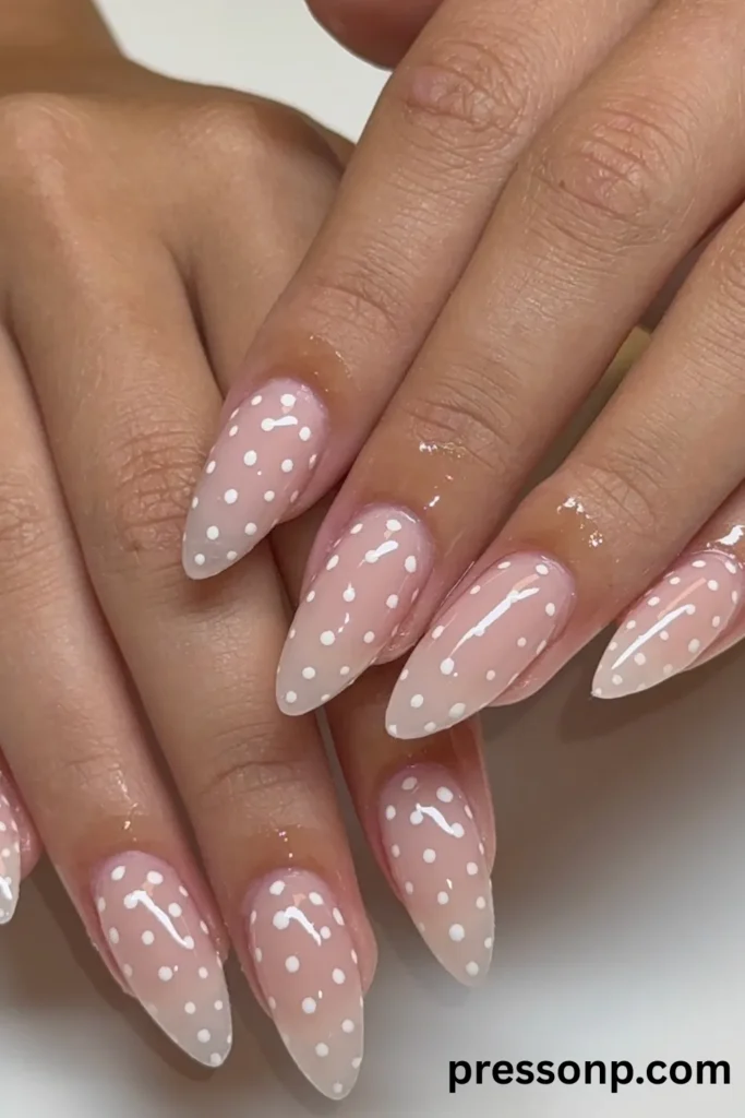 Close-up of long almond-shaped nails featuring a glossy, sheer clear base covered in a neat pattern of crisp white polka dots.