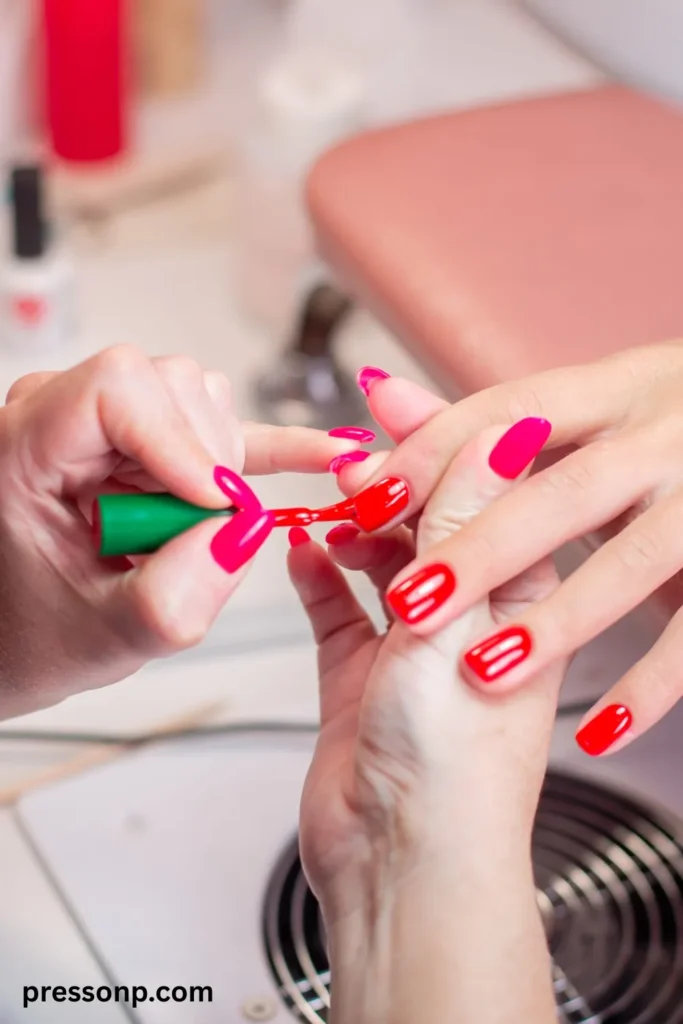 A close-up of a client receiving a professional salon manicure, where a nail technician uses a green-capped brush to apply a vibrant, glossy hot pink gel polish over long oval extensions.
