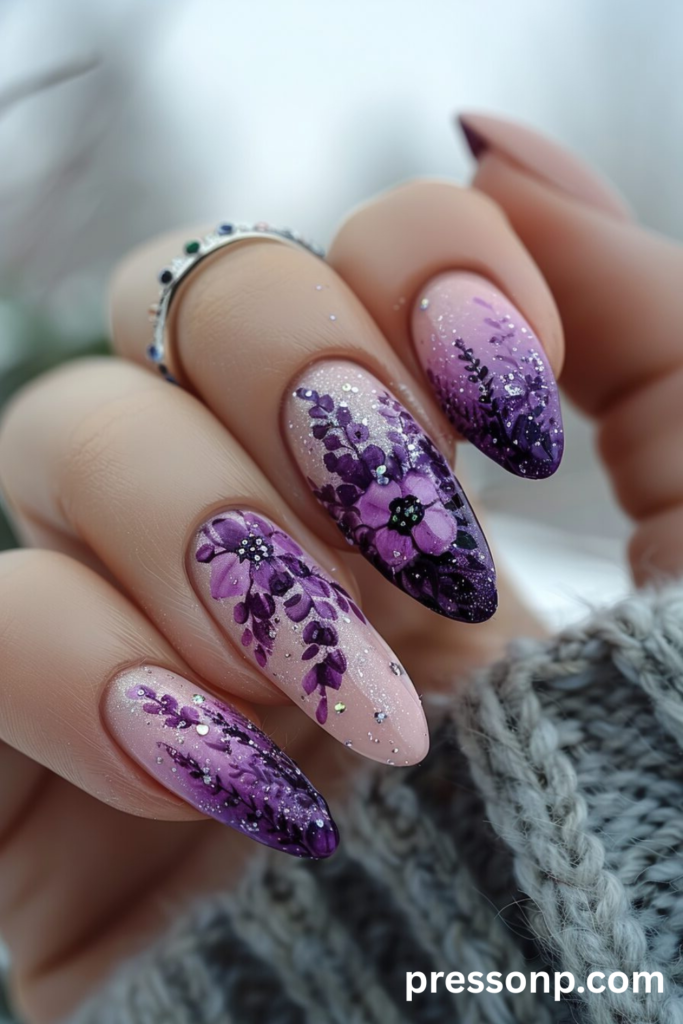 Close-up of long almond-shaped nails showcasing hand-painted "Wisteria Watercolor Nails" art with delicate purple blossoms, a soft pink-to-lavender gradient base, and fine silver glitter details.