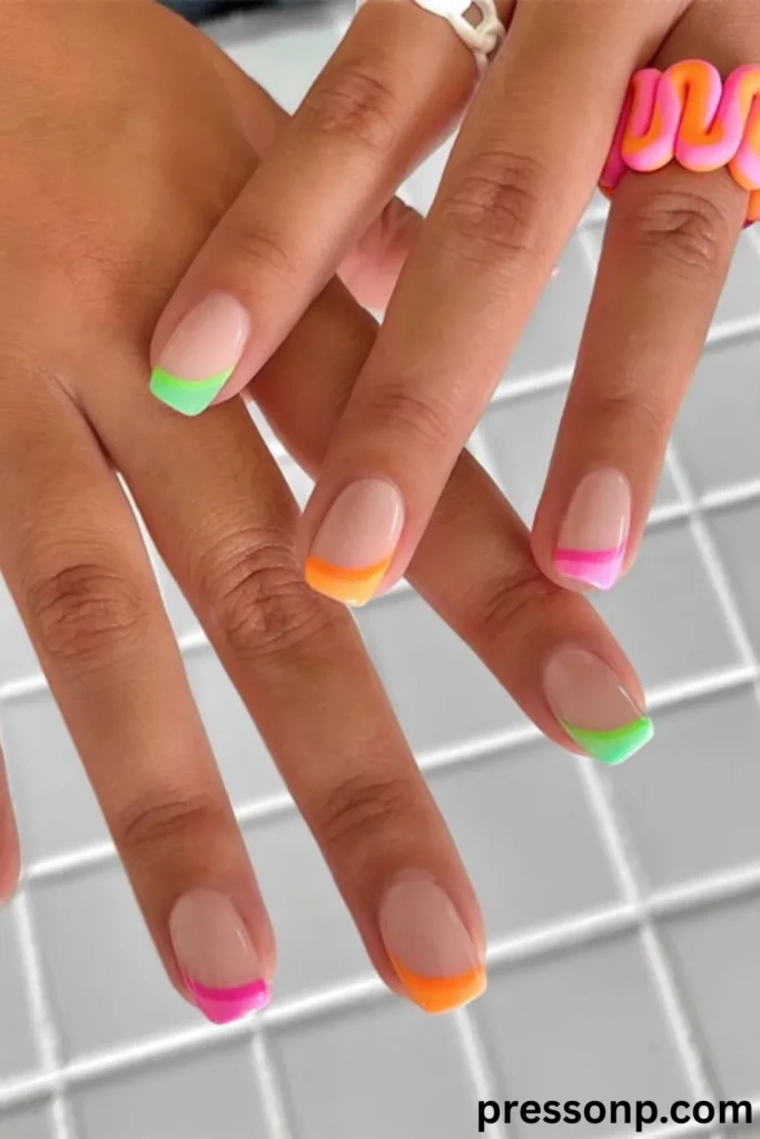 A close-up of hands displaying a colorful summer skittle French manicure on natural-length square nails, featuring a clean nude base paired with vibrant, dual-toned neon curved tips in shades of pink, orange, and lime green.