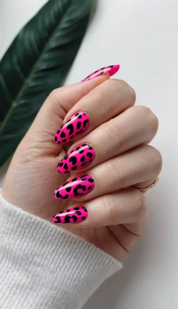 Close-up of long, glossy almond-shaped nails coated in a highly saturated neon hot pink polish and covered in a bold black leopard spot print pattern.
