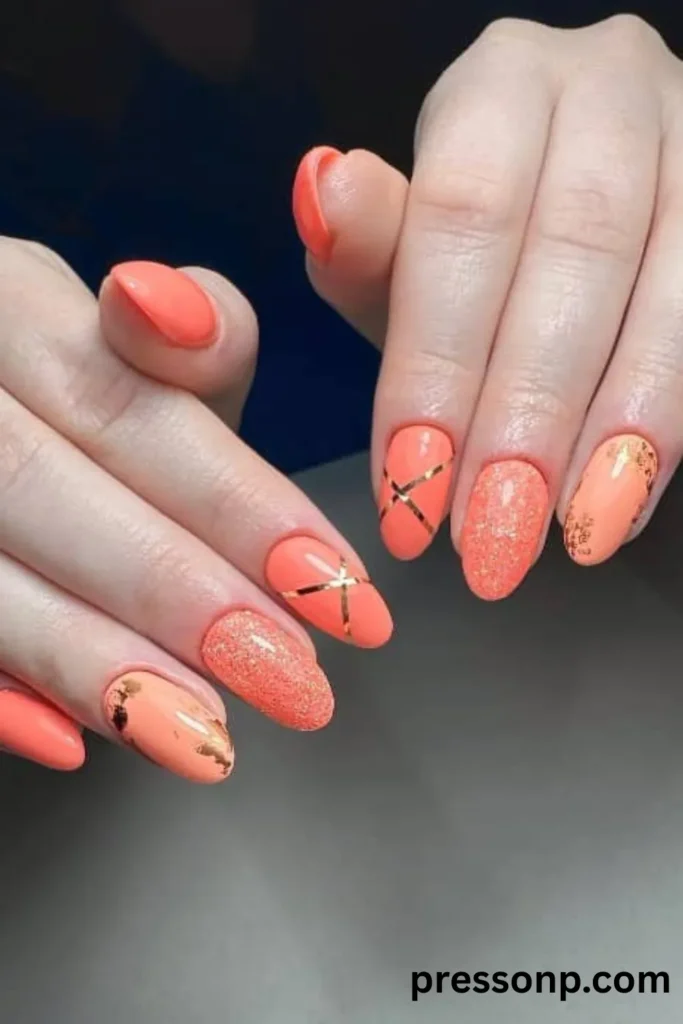 Close-up of hands with glossy oval-shaped nails showcasing a multi-design coral manicure featuring metallic gold striping tape, fine glitter coats, and distressed gold foil accents.